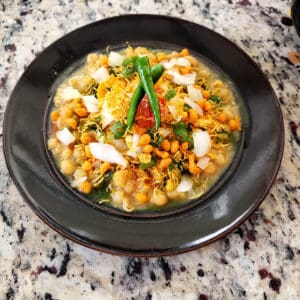 Matar Chaat served in black dinner plate with two green chilis and garnishes on top. This delicious Indian street food style curry is profusioncurry creation.