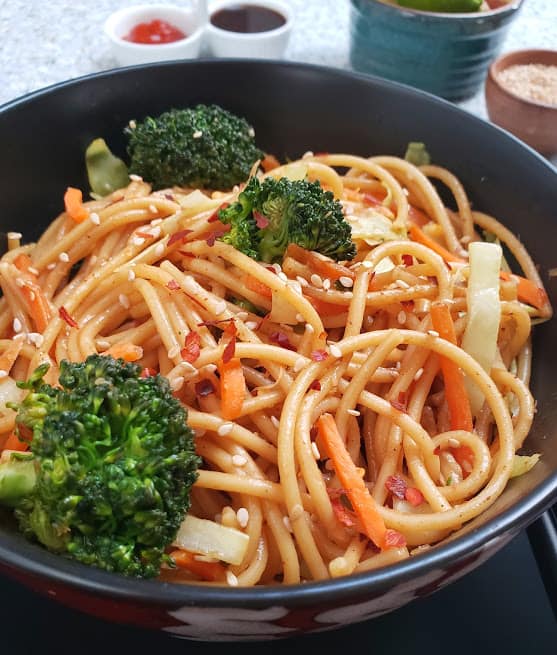 Chinese lo mein noodles served with colorful veggies and sesame garnish in a black container. This profusioncurry recipe can be made in Instantpot or stove top.