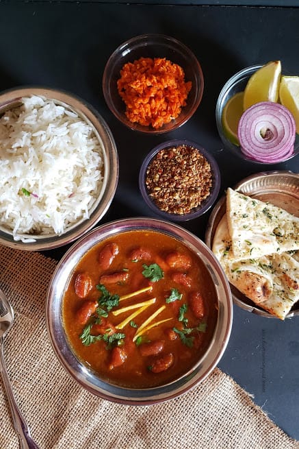 Indian dinner with Rajma masala curry, white rice, garlic naan, carrot pickle, flaxseed chutney and cut onions served in ethnic looking copper containers. 