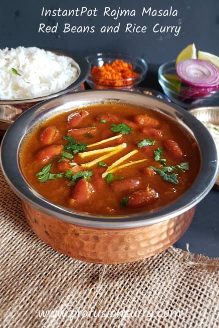 Ethnic copper serving container full of Rajma curry garnished with juliened ginger and chopped cilatro leaves. White basmati rice , red onion and lemon wedges in the background for complete dinner serving.