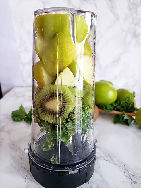 Un vaso frullatore a testa in giù riempito con ingredienti frullato verde crudo.