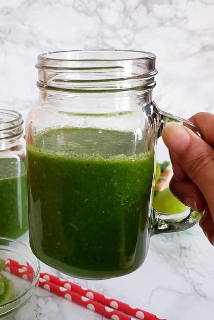 A hand holding a glass mason jar filled with green smoothie