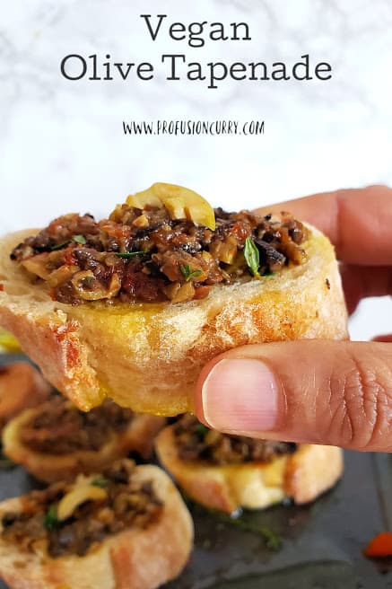 a hand holding a toast topped with olive tapenade.