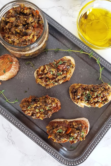 a rustic platter with several bread toasts topped with Vegan Olive Tapenade.