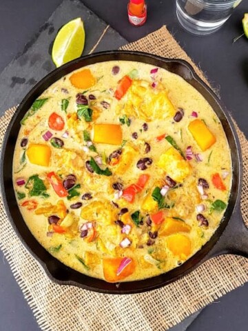 Colorful creamy butternut squash, black beans, bells peppers and spinach cooked in creamy stew served in cast iron skillet.