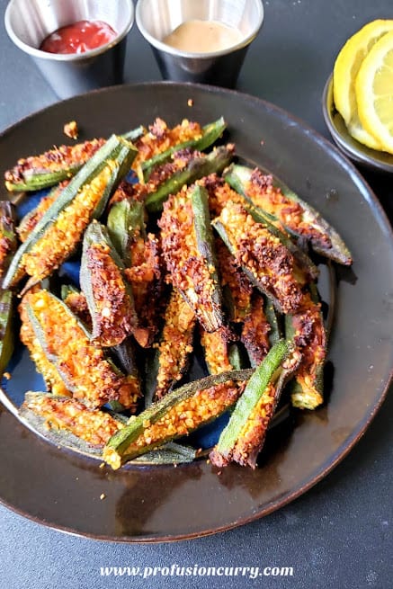 A black dinner plate full of stuffed okra along with two dipping sauces