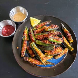 Crispy okra stuffed with ndian spices served on black dinner plate.