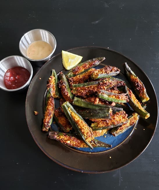 A black dinner plate full of stuffed okra, chutney and lemon.