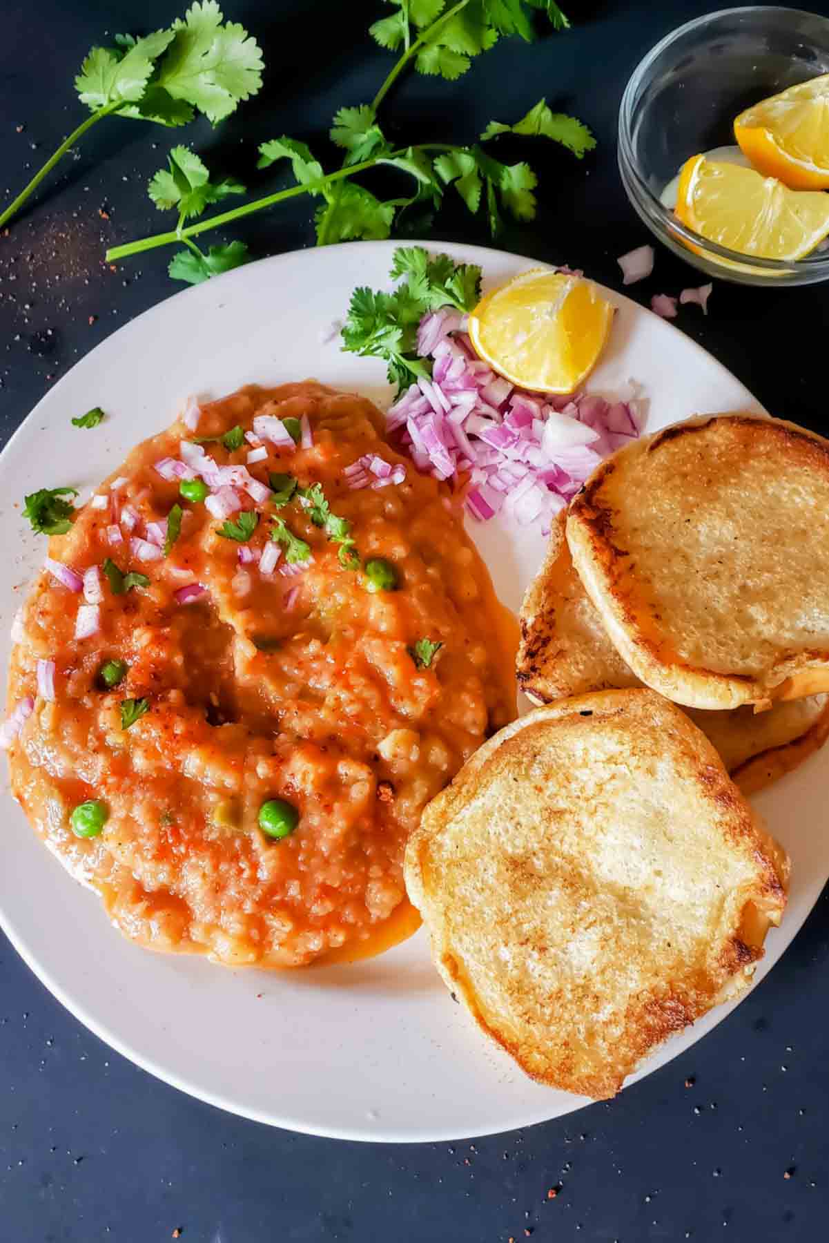 Instant Pot Pav Bhaji served with buttered pav, chopped onions, cilantro, and lemon wedges.