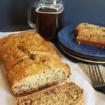 A sliced loaf of vegan banana bread on parchement paper with black coffee mason jar in the background.