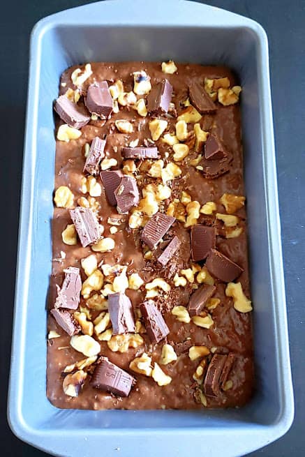 Chcolate banana bread batter poured in the loaf pan and garnished with walnuts and chopped chocolate pieces.