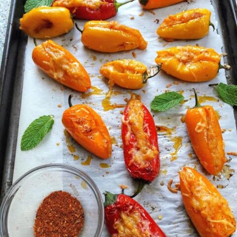 Cheese and potato stuffed peppers arranged on parchment paper and baking tray.