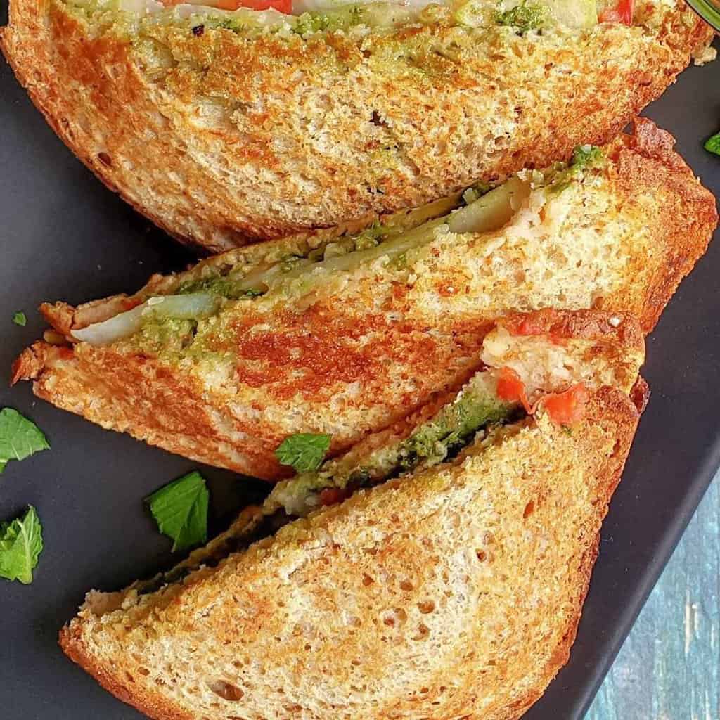 Toast sandwich made with bread, chutney and layered veggies served on black snack plate.