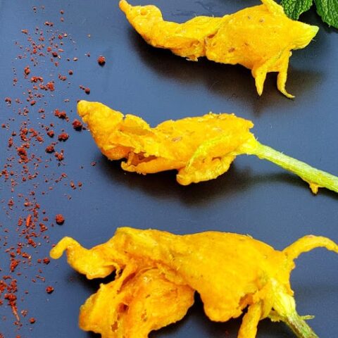 Indian style zucchini blossom fritters served on black serving platter with dry chutney