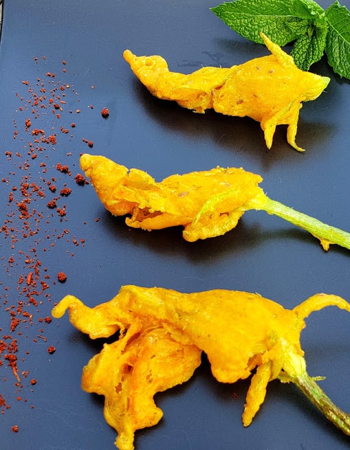 Indian style zucchini blossom fritters served on black serving platter with dry chutney