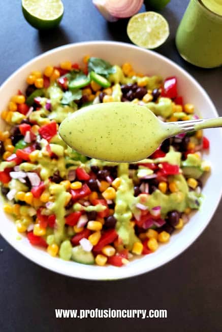 A spoon full of lime green avocado cilantro dressing ready to be drizzled over salad.