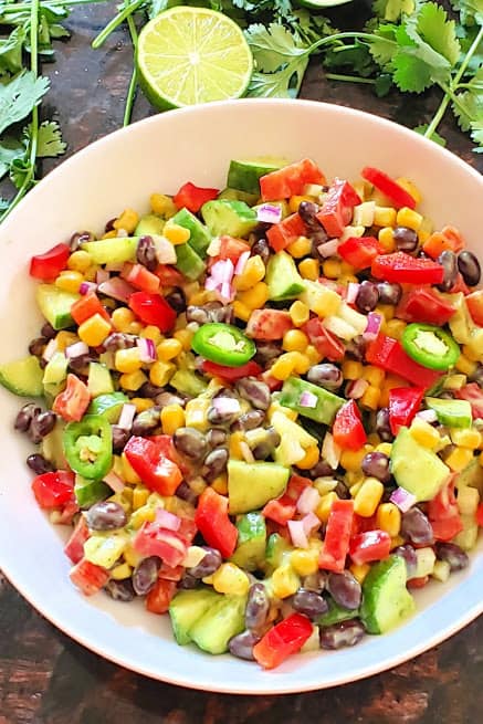 Black bean and corn salad along with avocado cilantro lime dressing served in a white salad bowl. This wholesome salad is perfect for summer lunches.