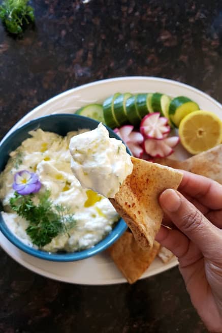 A hand holding pita bread triangel dipped in thick yogurt cucumber sauce.