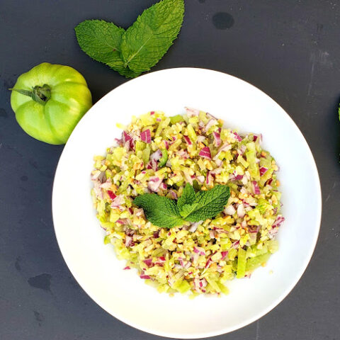 A salad plate full of green tomatoes and red onions and crushed peanuts mixed together to make refreshing garden fresh salad. This salad is full of garden fresh vegetables.