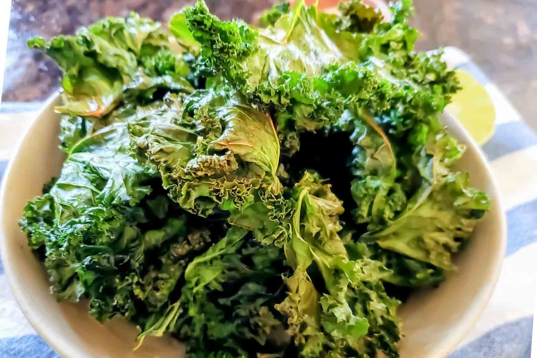 Crispy baked kale chips served in a white bowl with sea salt seasoning.
