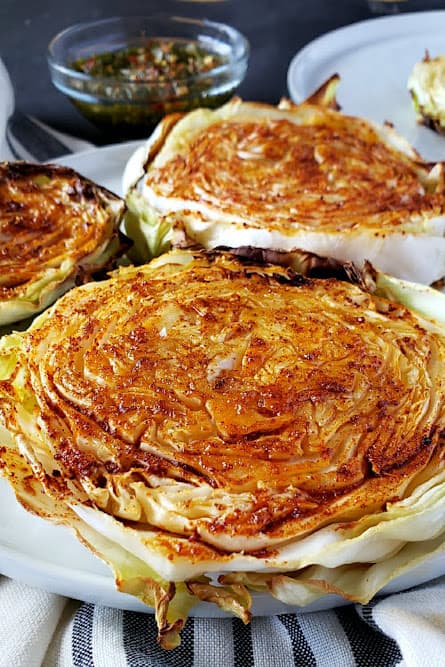 Three pieces of roasted cabbage served with cilantro chimichurri sauce served on dinner plate.