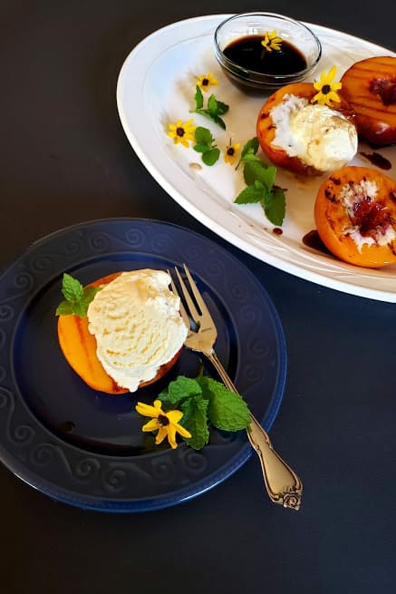 Grilled peaches served with vanilla nice cream in blue dessert plate.