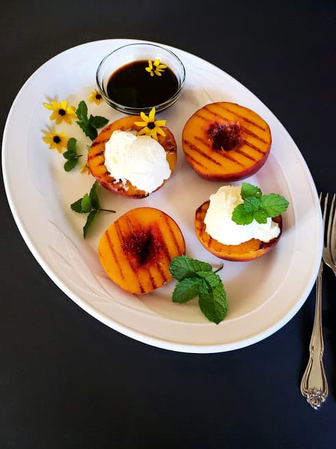 grilled peaches topped with dollop of ice cream garnished with mint and edible flowers.