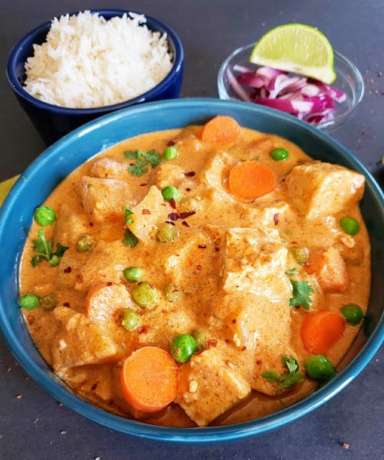 Un primer plano mostrando el lujoso y cremoso curry de coco amarillo con guisantes, zanahorias y patatas.