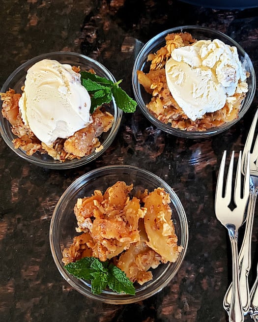 Apple Crisp dessert served in three small dessert bowls with coconut cream and ice cream dusted with cinnamon powder.