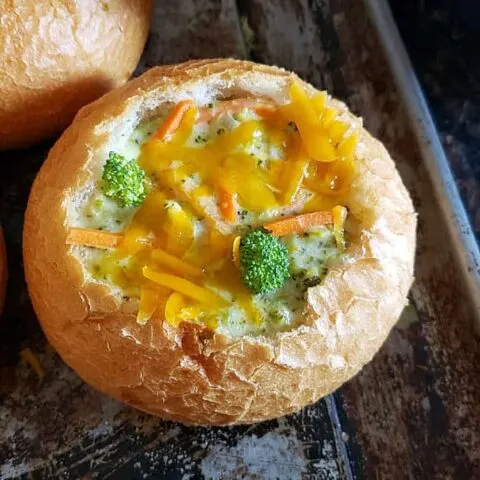 A bread bowl filled with Broccoli Cheddar Soup and garnished with frashly grated cheese.