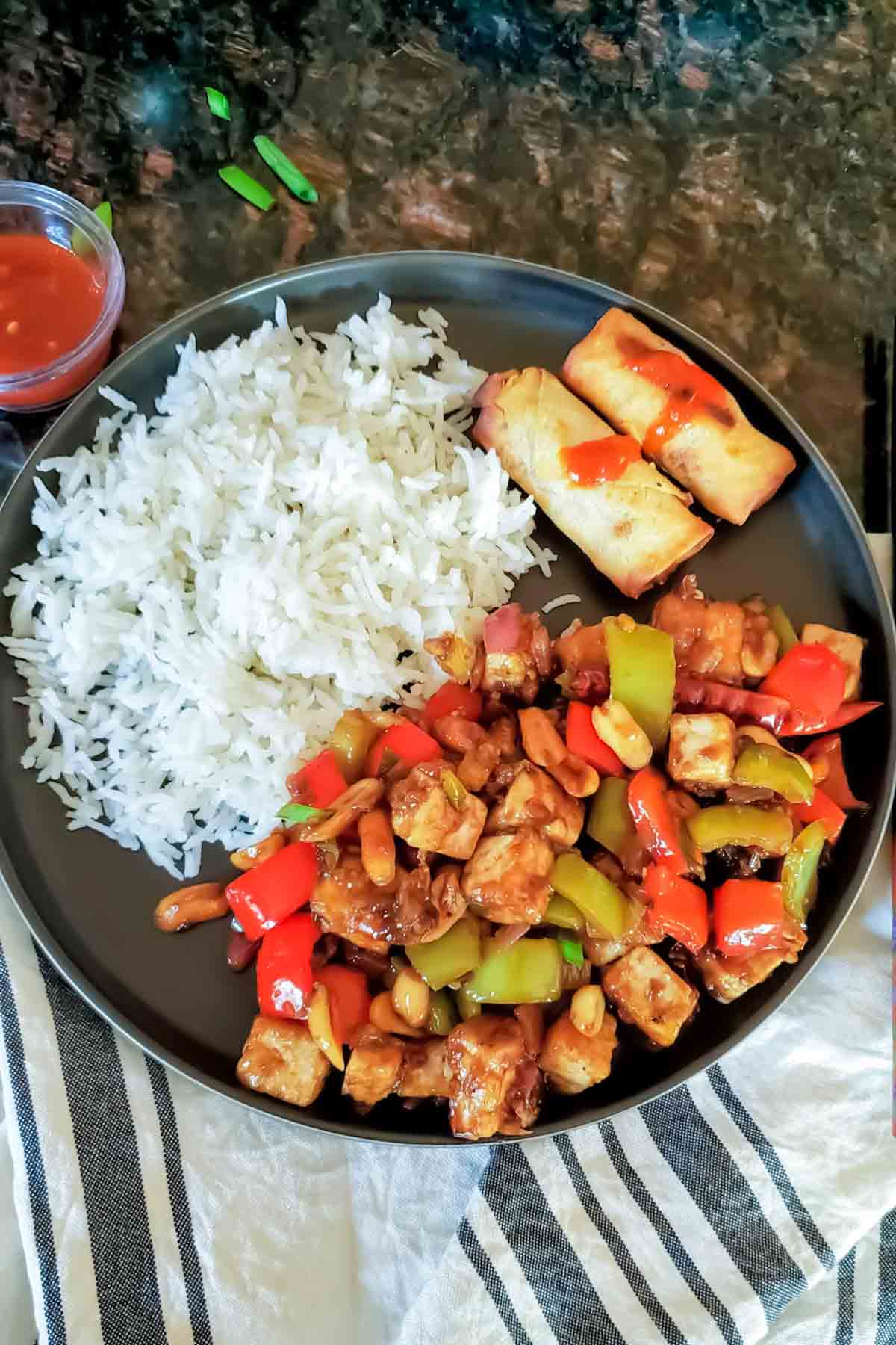 Asian dinner plate with homemade Kung Pao Tofu, rice and spring rolls. 