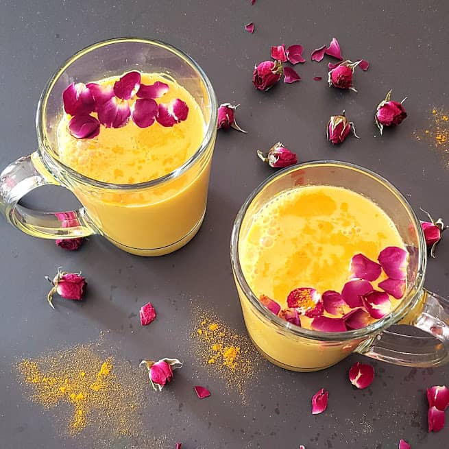 Two glasses filled with homemade turmeric latte served with rose petal garnishes.