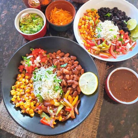 A dinner serving of two plates with colorful tex mex ingredients. These tortilla less Vegetarian Burrito Bowls are filling and flavorful.