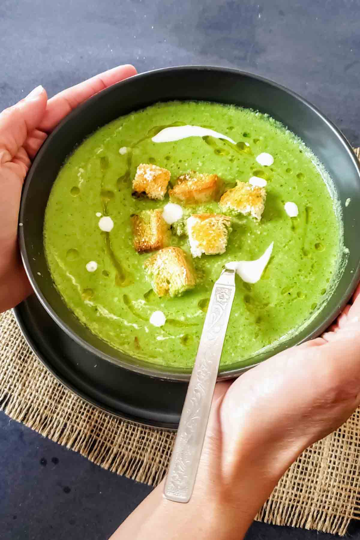 A hand holding a bowl of light and refreshing asparagus soup.