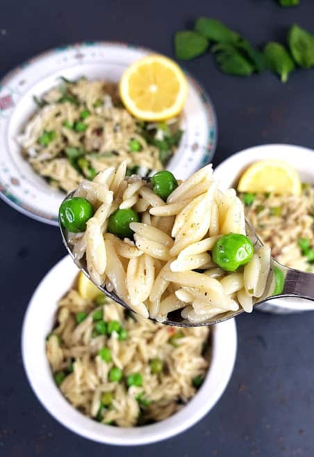 A spoon showing texture of peas and orzo pasta.