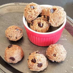 A red bowl filled with almond flour chocolate chip edible cookie dough balls along with a serving tray.
