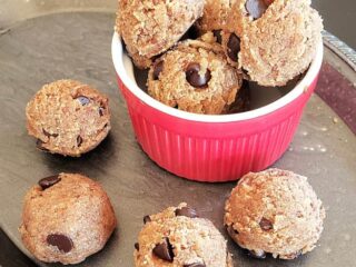 A red bowl filled with almond flour chocolate chip edible cookie dough balls along with a serving tray.