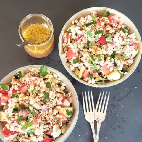 Two salad bowls filled with grain based barley salad with vegetables. Maple Dijon Mustard salad dressing is on the side.