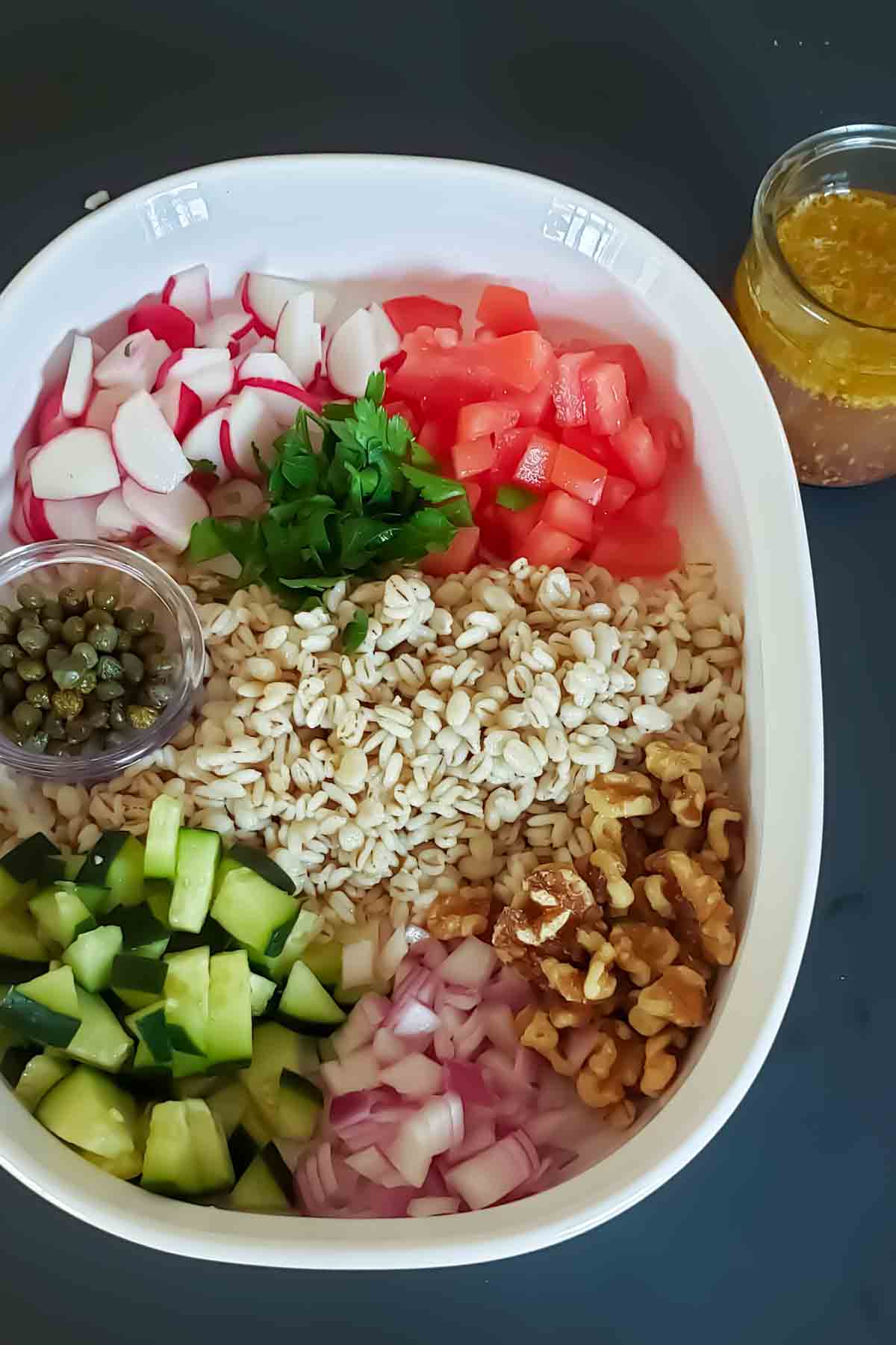 Making hearty barley salad with cooked pearl barley, crunchy veggies, walnuts, capers and maple, dejon, olive oil dressing.