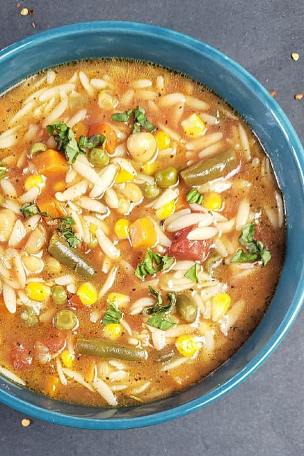 A blue bowl filled with vegetable pasta soup showing chunky hearty vegetables and rich brothy soup.