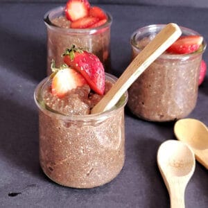 Chocolate chia seed pudding served in glass containers and topped with fresh strawberries for decadent healthy breakfast.