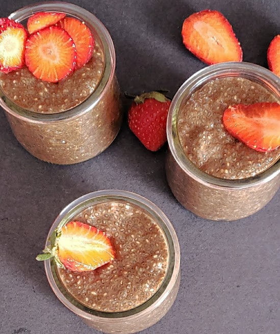 An overhead shot of 3 cups filled with chocolate pudding for breakfast topped with strawberries.