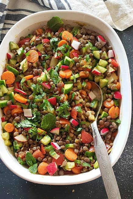 An overhead image showing a salad bowl full of lentil vegetable salad along with serving spoon.