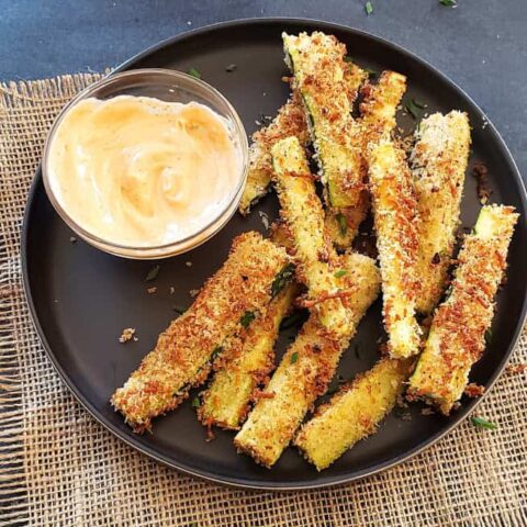 Air fried Zucchini fries served with a spicy mayo dip on the black serving plate.