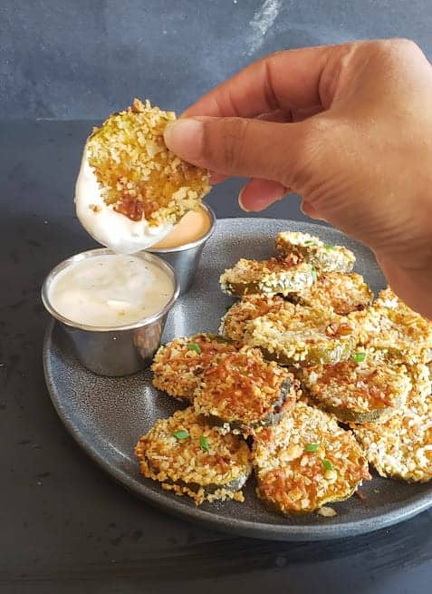 A hand holding fried pickle slice and dipping it in the sauce.