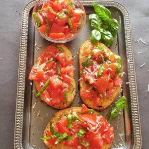 Tomato basil bruschetta served on bread toasts along with fresh basil and tomato mixture.