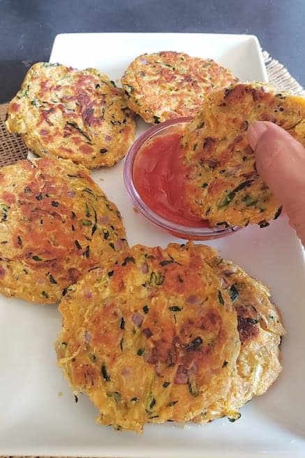 A hand holding a savory fritter and dipping it in the ketchup.