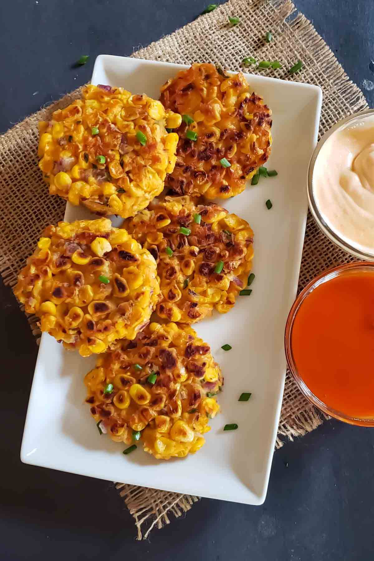 Crispy golden air fryer corn fritters on a plate with herbs.