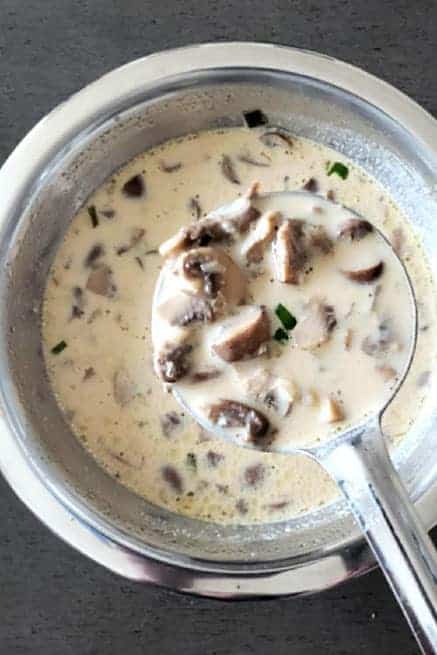 A ladle full of creamy soup with mushrooms. 