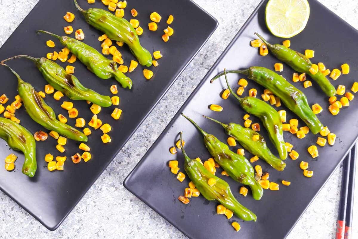 A black serving plate with blistered peppers and charred corn.